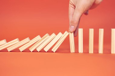 El parmağı düşmeyi durdurur. Tahta domino taşları, kırmızı arka plan, domino prensibi, iş konsepti.