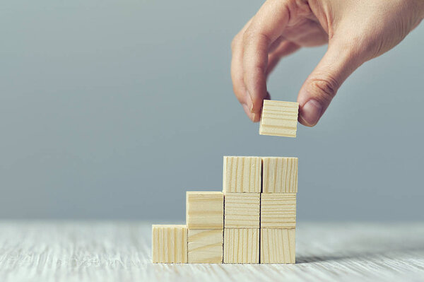 Hand arranging wood block stacking as step stair on wooden table. Business concept for growth success process. Copy space