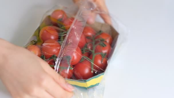 Жінка використовує харчову плівку для зберігання їжі на білому столі. вишневі помідори в одноразовій пластиковій упаковці. Повільне відео руху. крупним планом — стокове відео