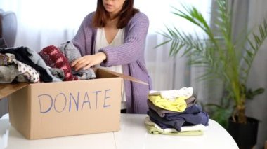 charity female at home put clothes into the cardboard box to donate. Shot video.