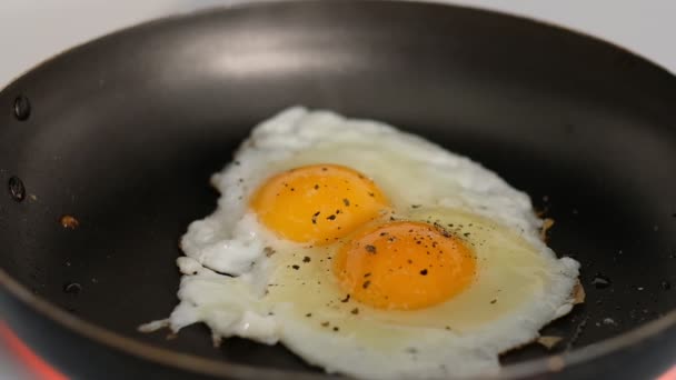 En kock steker ett ägg, solig sida upp, i en liten stekpanna över industriell gas brinnande spis med en grund skärpedjup. — Stockvideo