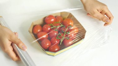 Beyaz bir masada yemek depolamak için yemek filmi kullanan bir kadın. Ürünleri paketlemek için şeffaf polietilen gıda filmi rulosu.
