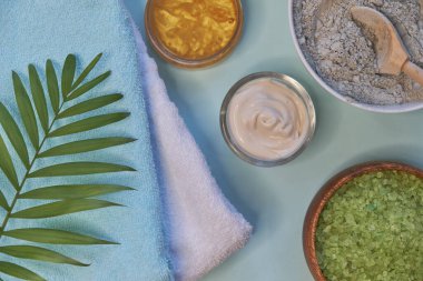Masaj kil tozu, yüz maskeleri, banyo tuzu, havlu, mavili tereyağı mavi masa arkasında..