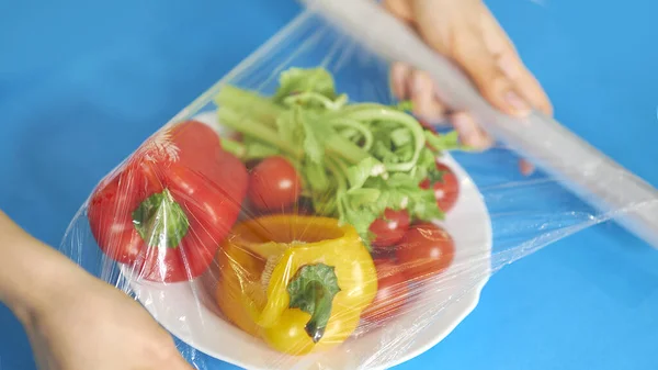 女人用食品膜把食物贮存在白桌上.包装产品用透明聚乙烯食品膜辊. — 图库照片