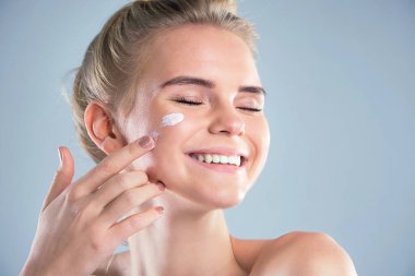 Yaz için nemlendirici güneş kremi. Güzel bir model yüzüne kozmetik krem sürüyor. Genç kadınların mutlu yüzü