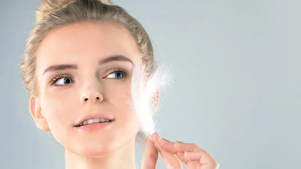 Retrato de chica atractiva con los ojos cerrados. hermosa mujer con una pluma blanca cerca de su cara. Concepto de cuidado de la piel de la cara y el cuerpo, piel brillante limpia fresca — Foto de Stock