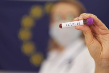 Doktor Avrupa Birliği bayrağının arka planında duruyor. Yeni Corona virüsü enfeksiyonu teşhisi için COVID-19 test ve laboratuvar örneği.