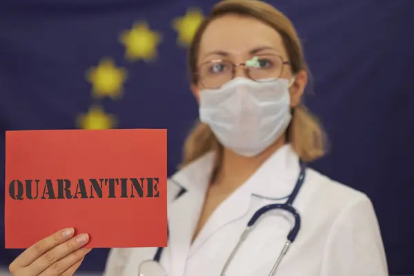 Doctor sostiene en sus manos una tarjeta roja la inscripción QUARANTINE en el fondo de la bandera de la Unión Europea. Novela coronavirus 2019-nCoV. Concepto de protección contra la pandemia viral —  Fotos de Stock