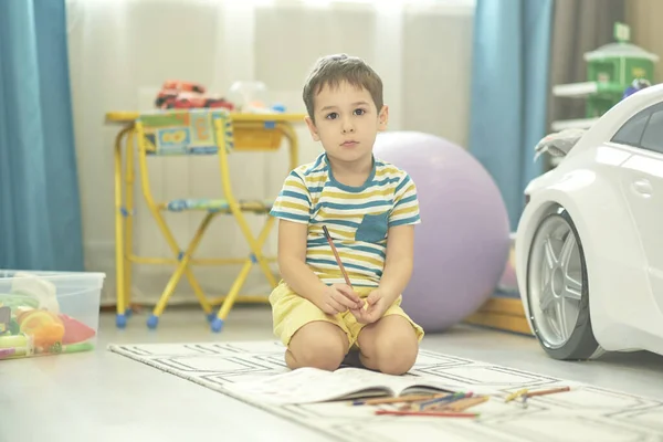 Egy imádnivaló fiú rajzol otthon a padlón. szomorú fiú ül a padlón a szobában — Stock Fotó