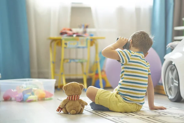 Kleine jongen speelt alleen in een kinderkamer en gebruikt een slimme huiskaart om te luisteren naar sprookjes. — Stockfoto