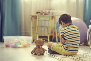 Üzgün çocuk bebek odasının zemininde oturuyor. Yalnız çocuk evini özlüyor.