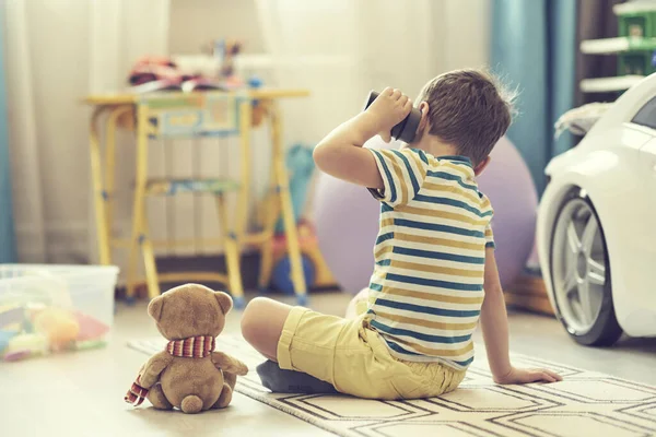 A kisfiú egyedül játszik egy gyerekszobában, és egy okos kártyával hallgatja a meséket.. — Stock Fotó