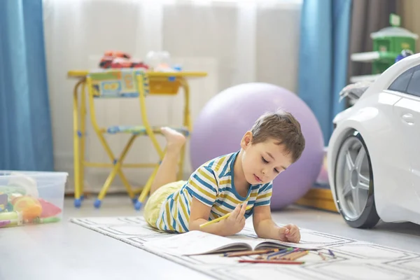 Egy imádnivaló fiú rajzol otthon a padlón. kis ázsiai fiú játszik a gyerekszobában, lágy tónusú, meleg színek. — Stock Fotó