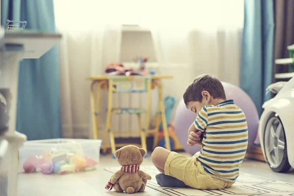 슬픈 소년 이 아기방 바닥에 앉아 있다. 외로운 아이가 집을 그리워해 — 스톡 사진