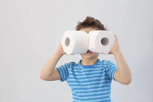Активный мальчик играет с туалетной бумагой в ретро-фильтре, мальчик смотрит через рулон унитаза, ребенок держит две белые ткани, Концепция охраны здоровья детей — стоковое фото