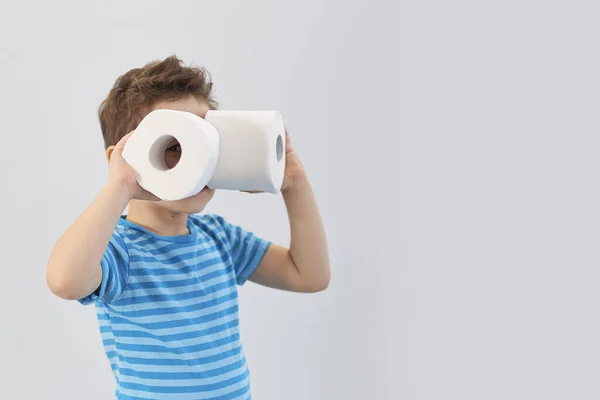 Ativo menino brincando com papel higiênico em filtro retro, garoto olhando através de rolo de vaso sanitário, criança segurando dois tecidos brancos, olhando através de papel higiênico como binóculos — Fotografia de Stock