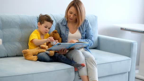 ママと息子はリビングでターコイズソファに座っている本を読んでいます. — ストック動画