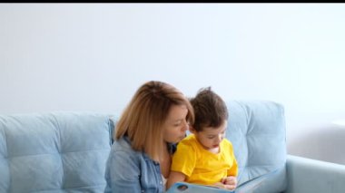 Anne ve oğlu oturma odasındaki turkuaz koltukta oturmuş kitap okuyorlar..