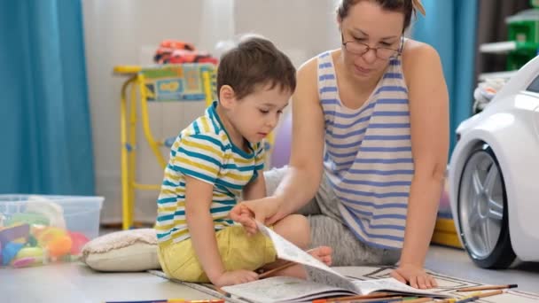 Junge glückliche Mutter und kleiner Sohn liegen auf dem Boden im Kinderzimmer und basteln und zeichnen zusammen — Stockvideo