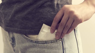 Kot pantolonun cebinde prezervatif. Kız kot pantolonun cebine el prezervatifi koyuyor. Kapat..