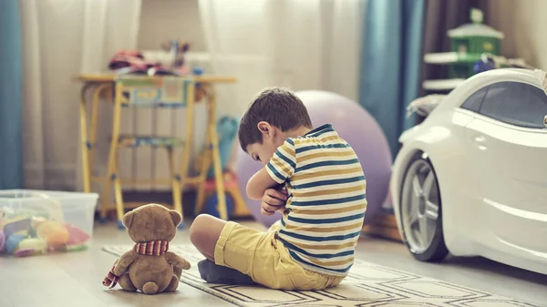 Το θλιμμένο αγόρι κάθεται στο πάτωμα του παιδικού σταθμού. Το μοναχικό παιδί λείπει σπίτι — Φωτογραφία Αρχείου