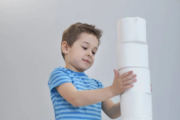 Boy builds a tower of toilet paper. Active boy playing with toilet paper in retro filter. Child hugs a bunch of toilet paper, Children health care concept — Stock Photo, Image