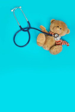 Doldurulmuş oyuncak ayı hayvanı, elinde stetoskop ve mavi izole arka planda fotokopi alanı olan bir çocuk doktoru olarak sunuluyor.