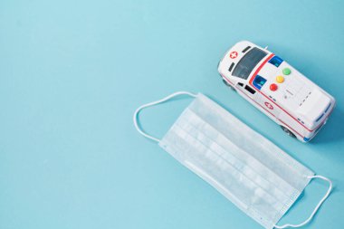 Oyuncak ambulansı kapatın ve mavi arka planda koruyucu maske takın..