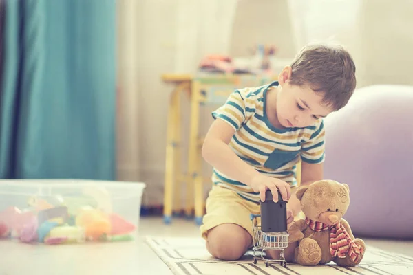 A kisfiú egyedül játszik egy gyerekszobában, és egy okos kártyával hallgatja a meséket.. — Stock Fotó