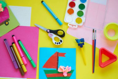 Okul malzemeleri, sarı arka planda kırtasiye malzemesi - manşet için yer. Çocuk kalemle çizmeye ve renkli kağıt uygulamaya hazır. Üst görünüm.