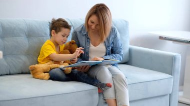 Anne ve oğlu evdeki kanepede kitap okuyorlar.