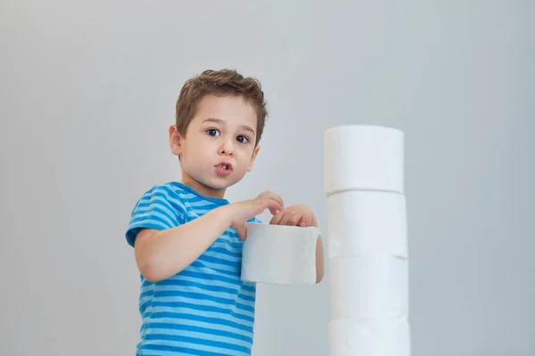 Boy builds a tower of toilet paper. Active boy playing with toilet paper in retro filter. Child hugs a bunch of toilet paper, Children health care concept — Stock Photo, Image