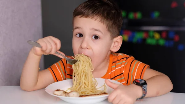 Engraçado menino comer macarrão na mesa da cozinha . — Fotografia de Stock