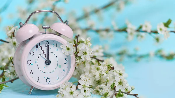 Pembe çalar saat ve mavi arka planda küçük beyaz çiçekler. Üst Manzara. Sevgi ve selamlama zamanı. Bahar Zamanı Değişimi, Bahar Çiçekleri ve Alarm Saati. — Stok fotoğraf