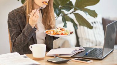Tanımlanamayan genç iş kadını masada öğle yemeği molası veriyor. Taze salata yiyor.