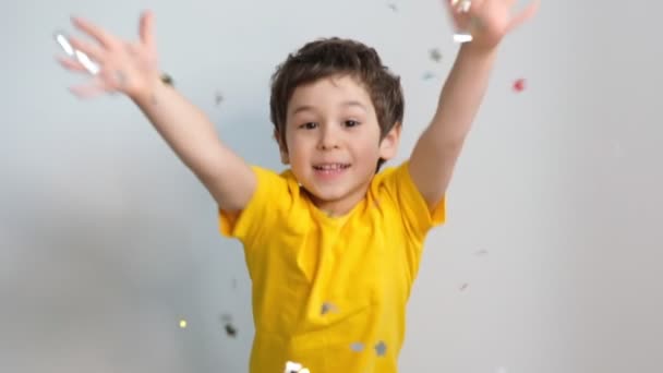 Gelukkige verjaardag kind. Foto van charmante leuke fascinerende kleine jongen blazen confetti naar u om haar feestelijke stemming te laten zien met emotionele gezicht uitdrukking. Beelden. Slow Motion video. Sluiten. — Stockvideo