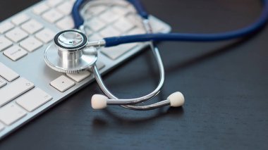 Gümüş steteskop siyah arka planda, beyaz klavyede yatıyor. Stok fotoğrafı. uzak tanımlamalar