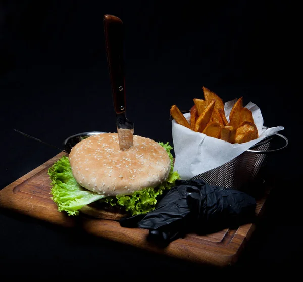 美味的烤牛肉汉堡配生菜, 芝士和洋葱, 在一张黑色的木桌上用法式薯条在切板上上菜。 — 图库照片