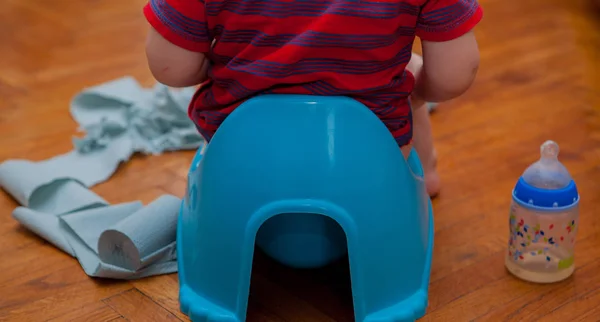 Little baby sitting on chamber pot with toilet paper and pacifier on a brown background — Stock Photo, Image