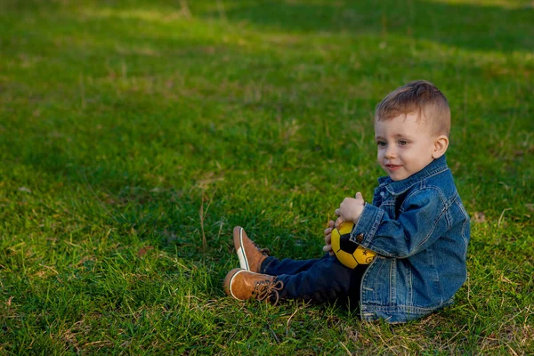 Двухлетний мальчик держит футбольный мяч сидя на траве — стоковое фото