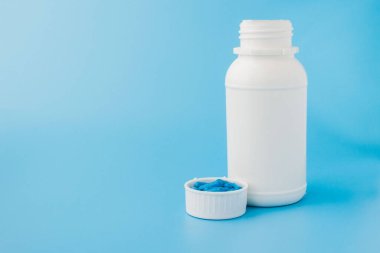 Mavi kapsüller, mavi arka planda haplar. Beyaz kavanozdaki kapsüller. Vitaminler, kadın sağlığı için besin takviyeleri