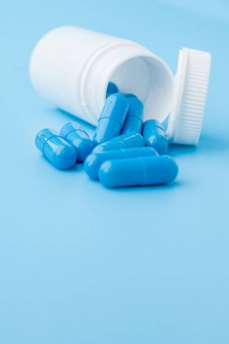 Mavi kapsüller, mavi arka planda haplar. Beyaz kavanozdaki kapsüller. Vitaminler, kadın sağlığı için besin takviyeleri