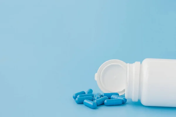 Cápsulas azules, pastillas sobre fondo azul. Cápsulas en un frasco blanco. Vitaminas, suplementos nutricionales para la salud de las mujeres — Foto de Stock