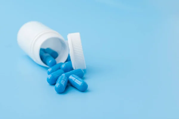 Cápsulas azules, pastillas sobre fondo azul. Cápsulas en un frasco blanco. Vitaminas, suplementos nutricionales para la salud de las mujeres — Foto de Stock