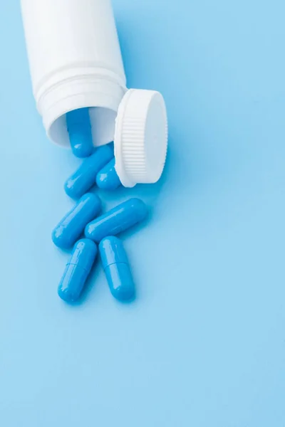 Cápsulas azules, pastillas sobre fondo azul. Cápsulas en un frasco blanco. Vitaminas, suplementos nutricionales para la salud de las mujeres — Foto de Stock