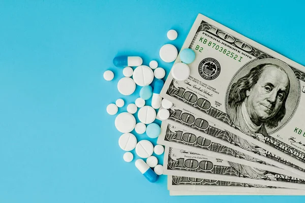 Розкидані фармацевтичні ліки таблетки, таблетки та капсули на доларах гроші ізольовані на синьому фоні. Витрати на медицину . — стокове фото