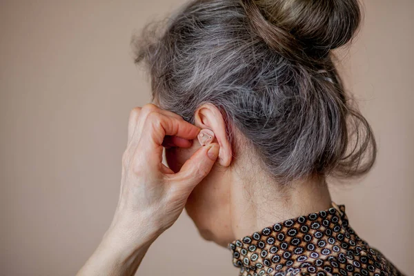 Close-up mulher sênior inserindo aparelho auditivo em seus ouvidos — Fotografia de Stock