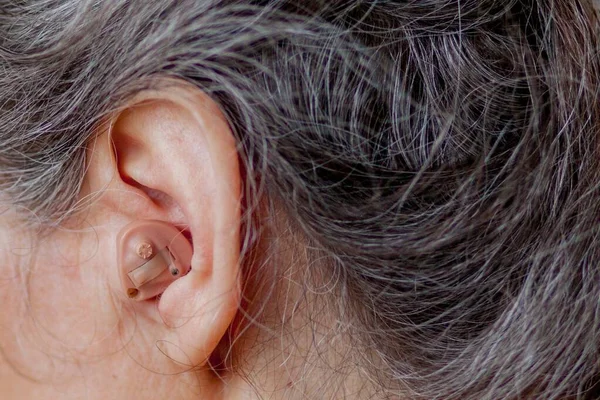 Closeup senior woman inserting hearing aid in her ears — Stock Photo, Image