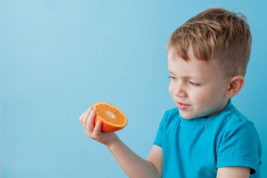 Mavi arka planda elinde portakal tutan küçük çocuk, iyi sağlık kavramı için diyet ve egzersiz yapıyor.