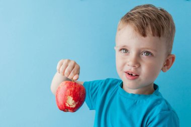 Bebek kucağında kırmızı elma, mavi arka plan, yemek, diyet ve sağlıklı beslenme konsepti